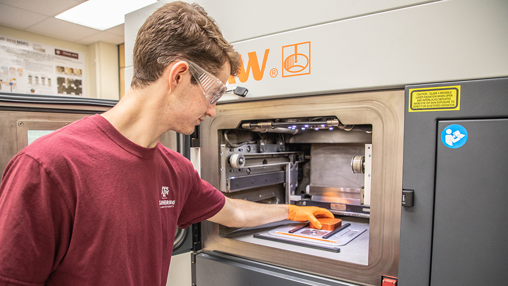 Student placing a metal object inside a large metal additive 3D printer.