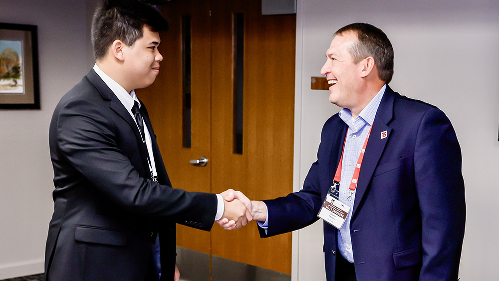 Two smiling men in professional attire shaking hands.