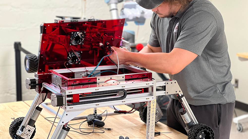 A student works on the system board for a robot on wheels.