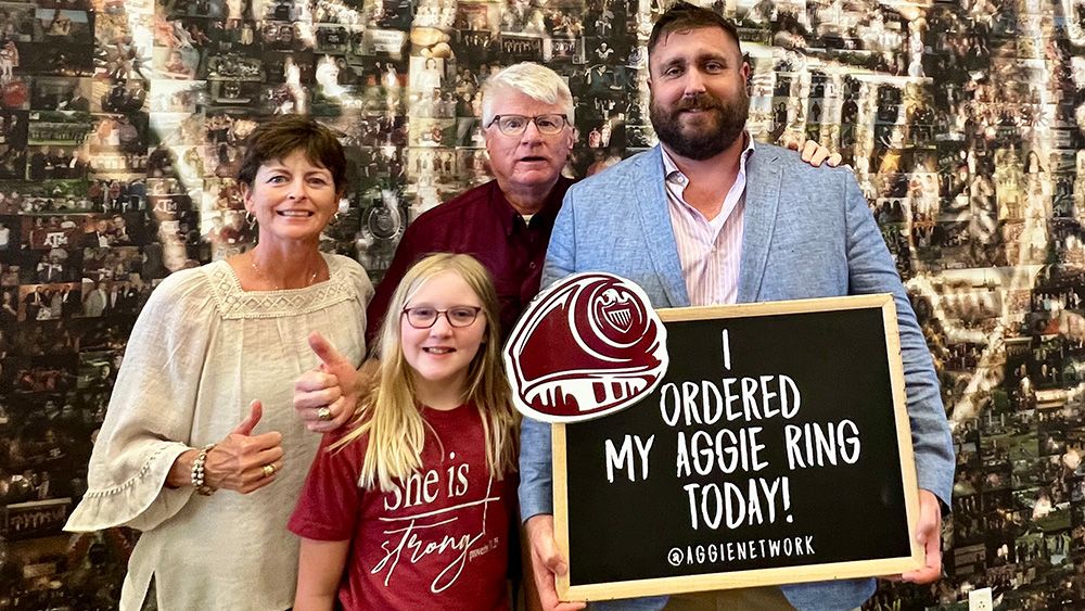 older male student stands with mother, father, and daughter while holding sign stating "I ordered my Aggie ring today!"