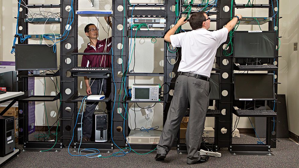 Wide shot of two men working with technology equipment rack.