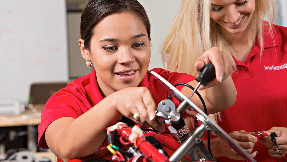Female student building motor with a tool.