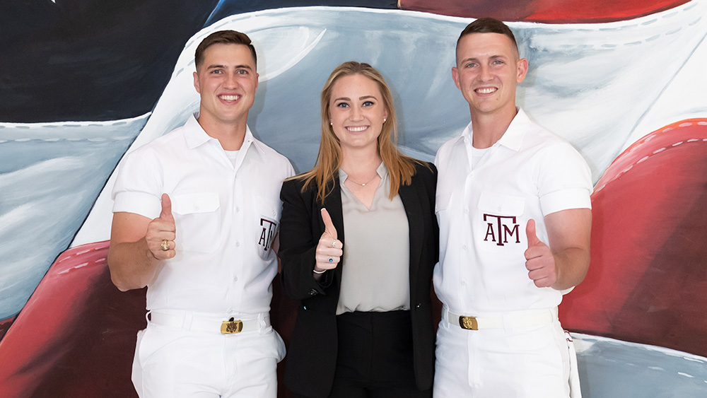 METM student posing with Texas A&amp;M spirit yell leaders holding Gig-em hand sign.