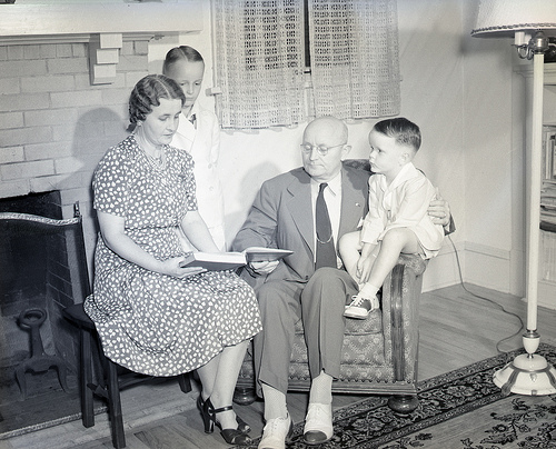 Ide Trotter sits in a chair and reads to his wife and children