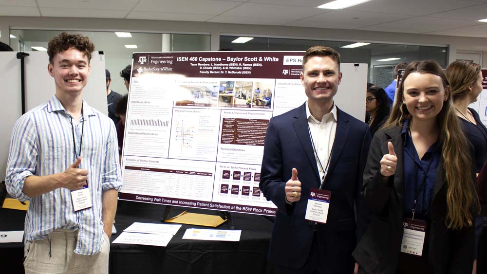 Three students stand by their presentation poster. All are smiling at the camera.