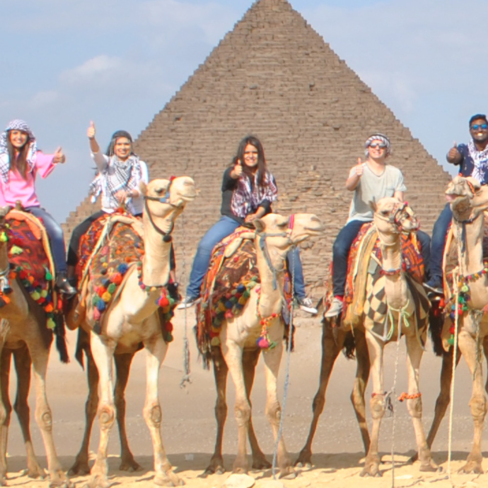 Students sitting on camels with the Great Pyramids in the background.
