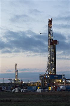 two Marathon Oil drilling rigs with lights on shown at dusk