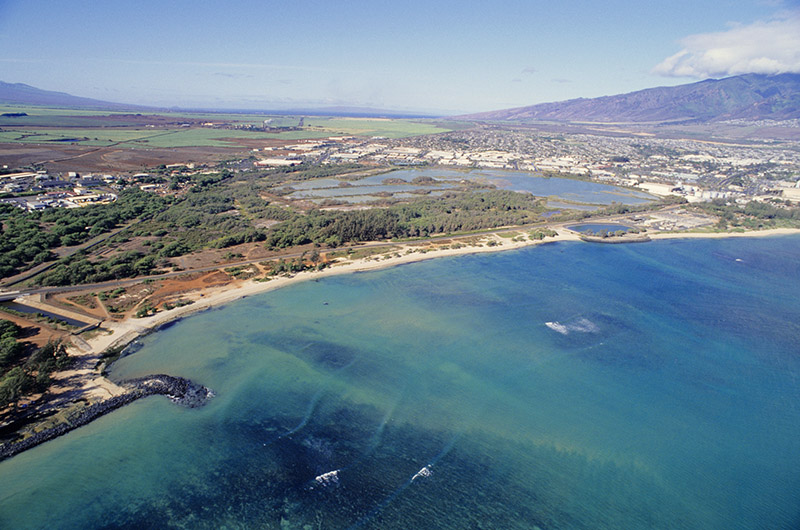 Aerial view of coast. Water is a blue green. Mountains can be seen in the distance. 