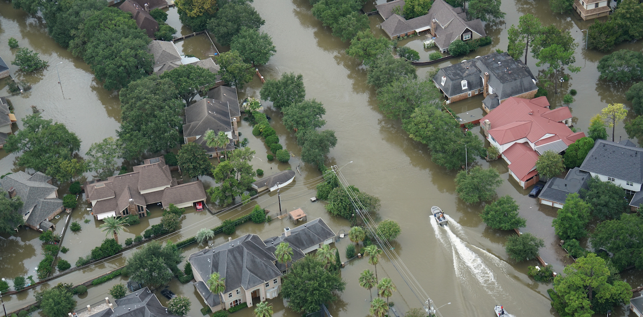Aerial view of a badly flooded neighborhood. A boat is being driven down what used to be the street.