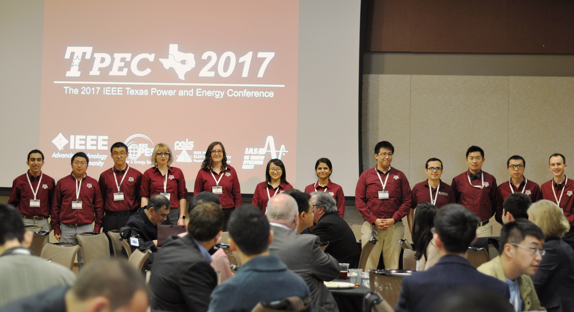 Group of students from the IEEE Power and Energy Society, Power Electronics Society and Industry Applications Society joint chapters standing up in front of conference attendees.