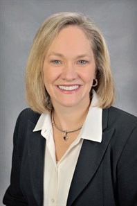 Woman with short blonde hair in a black blazer and white button up shirt with collar in formal portrait.