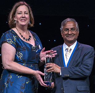 Janeen Judah and Akhil Datta-Gupta shown jointly holding approximately one foot tall clear acrylic sculpture award with dark base