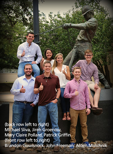 seven smiling students gathered around statue of rough neck on Texas A&amp;M campus