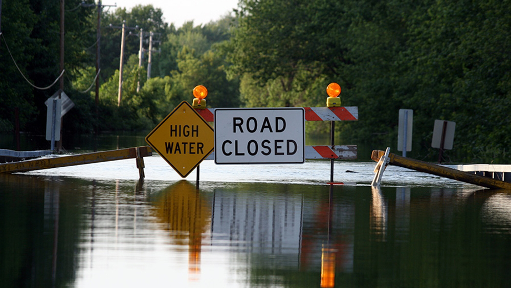 Two signs High Water and Road Closed in the middle of a flooded road
