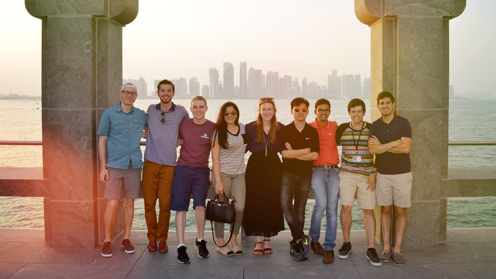 Group of Texas A&amp;M students in Qatar, posed in front of shore and city line. 