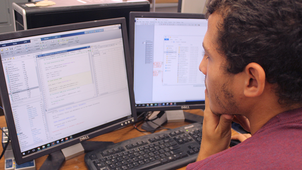 Ibrahim El-Sayed reviews feedback displayed on computer screens from the sensors of the small-scale drilling rig