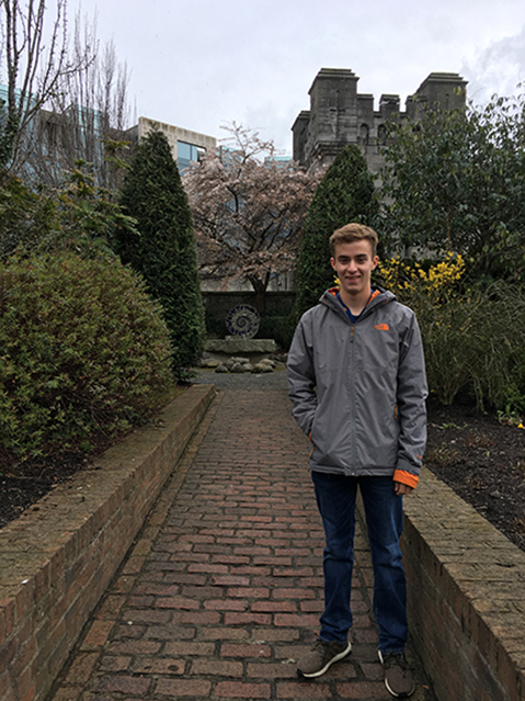 David Moore standing on brick sidewalk in garden with castle-like structure in the background.