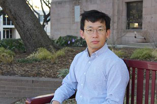 Jun Oh seated outdoors on a wooden bench located on Texas A&M campus