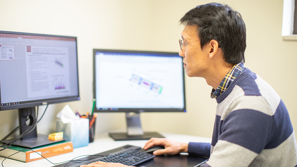 Dr. Kang is working at a desk with models of his research on the computer models.