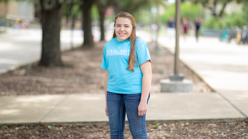 Patricia Rodriguez stands under trees on a sunny day wearing a blue Ocean Engineering shirt.