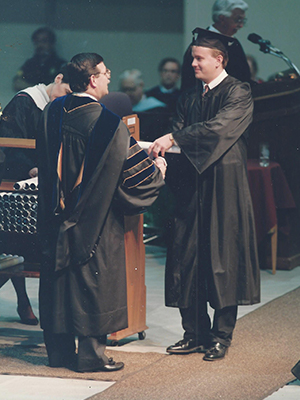 Dr. Brian Craig receives a diploma on stage at his undergraduate graduation. 