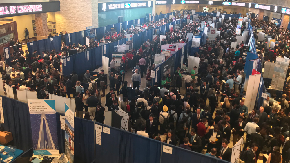 Large group of students among job recruiter booths at engineering career fair.