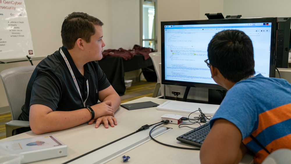 Two students working on coding assignment on a computer.