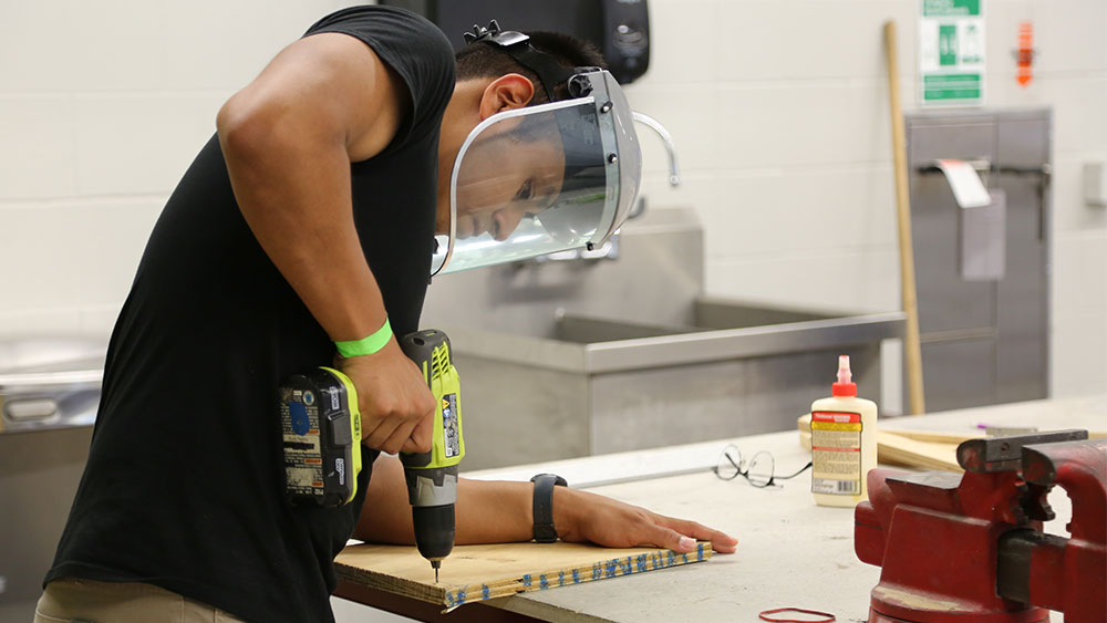 A student drilling into a board at Aggies Invent: Energy Solutions