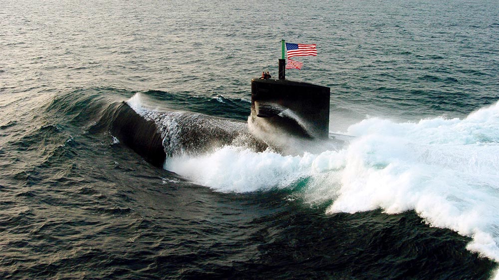 A submarine with an American flag flying breaches the ocean.