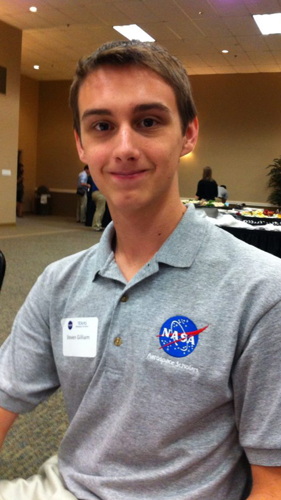 Steven Gilliam, a junior in high school at the time, smiles in his gray NASA polo while seated for dinner at NASA’s High School Aerospace Scholars program.