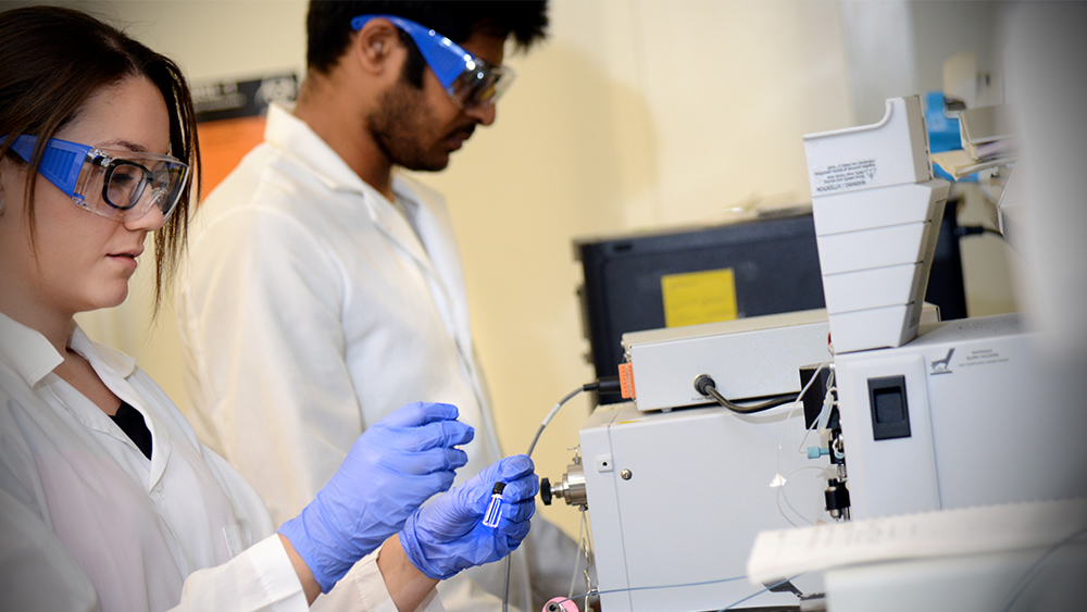 Two students in lab gear working in a chemical engineering lab.