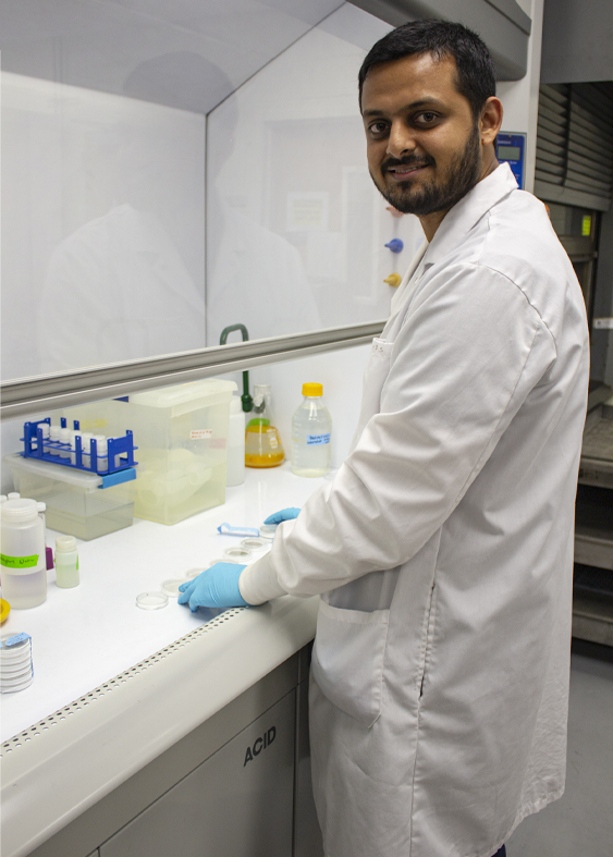 Doctoral student Sourav Das, wearing a long white coat, works in a lab analyzing dust samples. 
