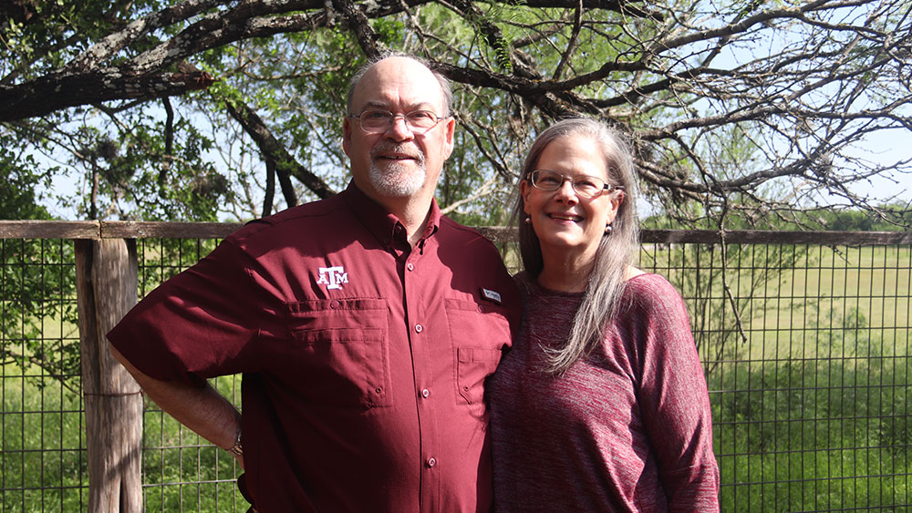 Keith and Lee Coleman '81 stand and pose in front of a tree and fenced pasture.