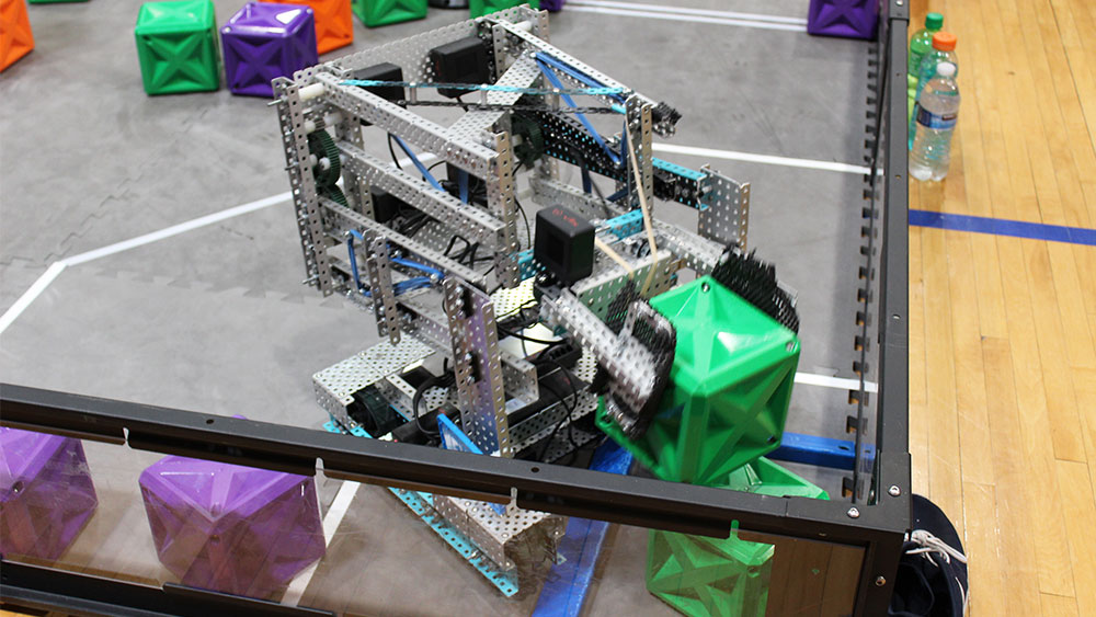 VEX robot picking up cubes in the competition arena.