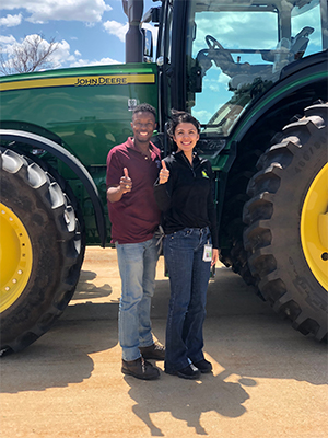 Two students stand in front of tractor. 