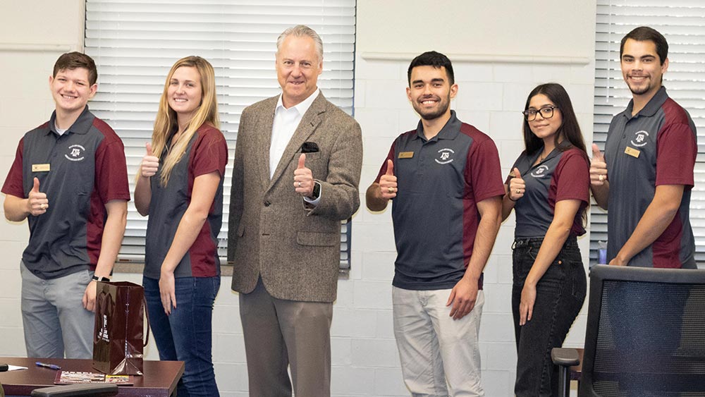 A group of students pose with Craig Piercy and do a "gig 'em" hand gesture. 