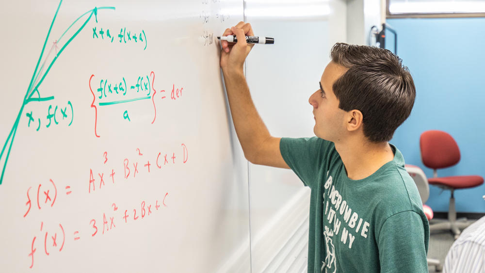 A student solving a math problem on a whiteboard