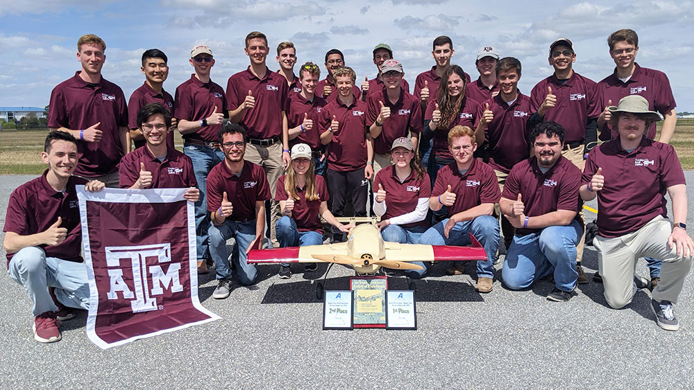 TAMU SAE team, Farmers Flight, posing next to their aircraft and awards on the runway at competition.