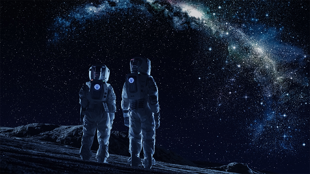 Two astronauts stand on the moon looking at the milky way. 