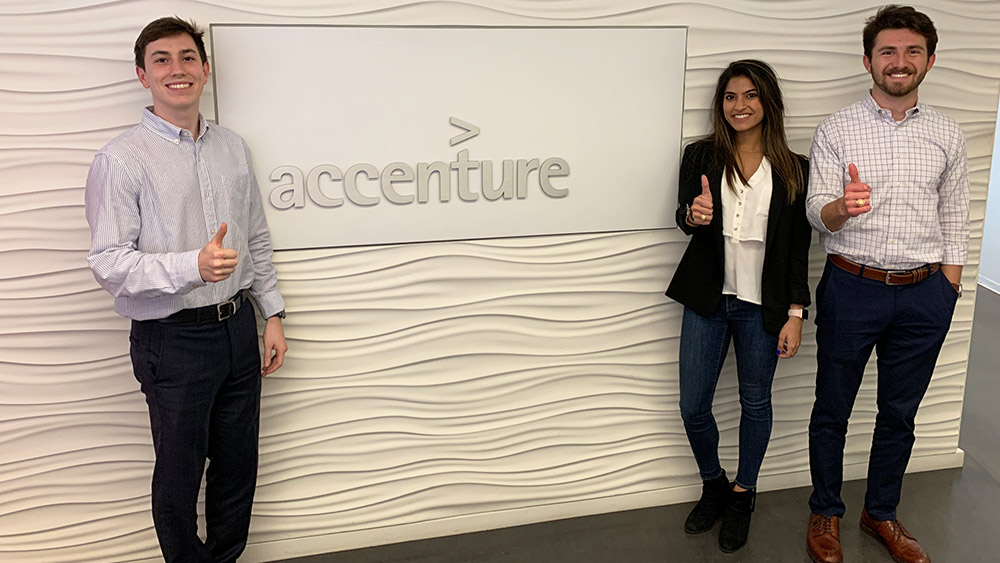 Team smiling in front of Accenture sign.