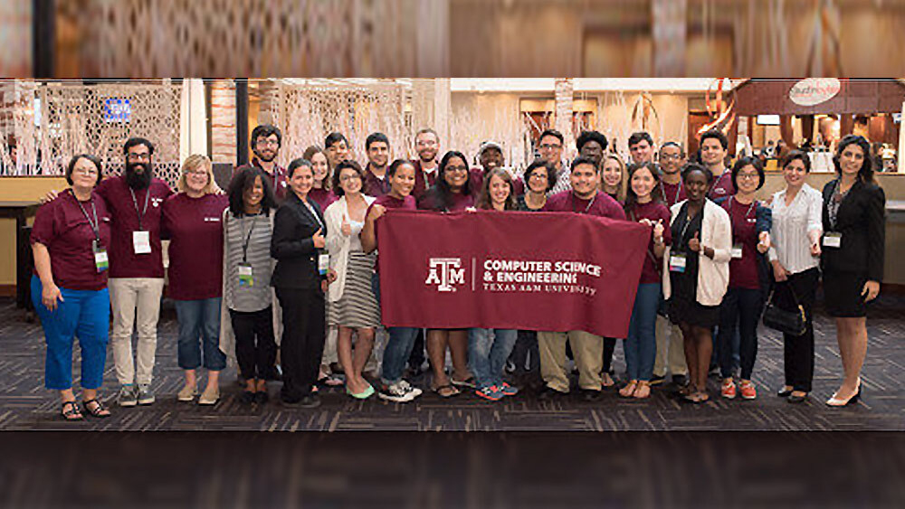 Large group of students from the Aggie Hispanics in Computing group with their mentors. The students in the front of the group are holding up a large maroon cloth that has the Department of Computer Science and Engineering logo on it.