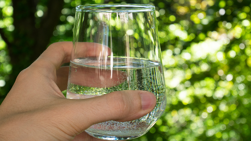 A man holds a glass of water against a background of trees