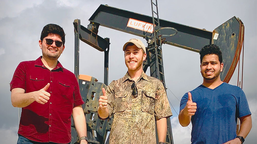 Graduate students posing in front of a pump jack.
