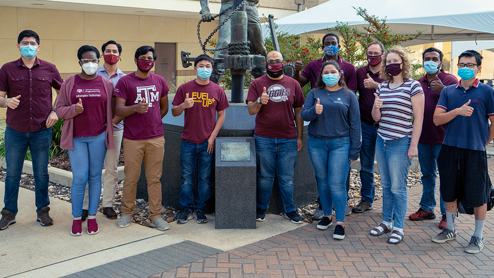 Mentor and several members of the Aggie 2020 NASA team wearing masks and giving thumbs up Gig-Em sign