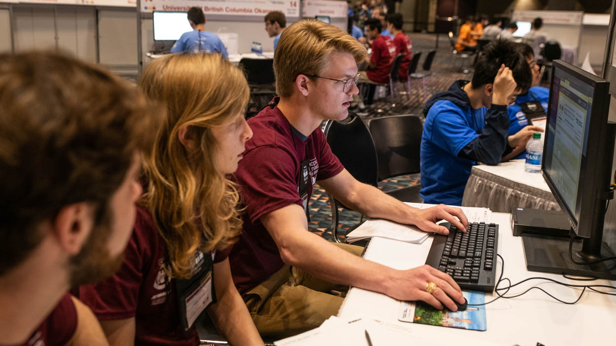 Three Texas A&M students practicing programming skills on computer.