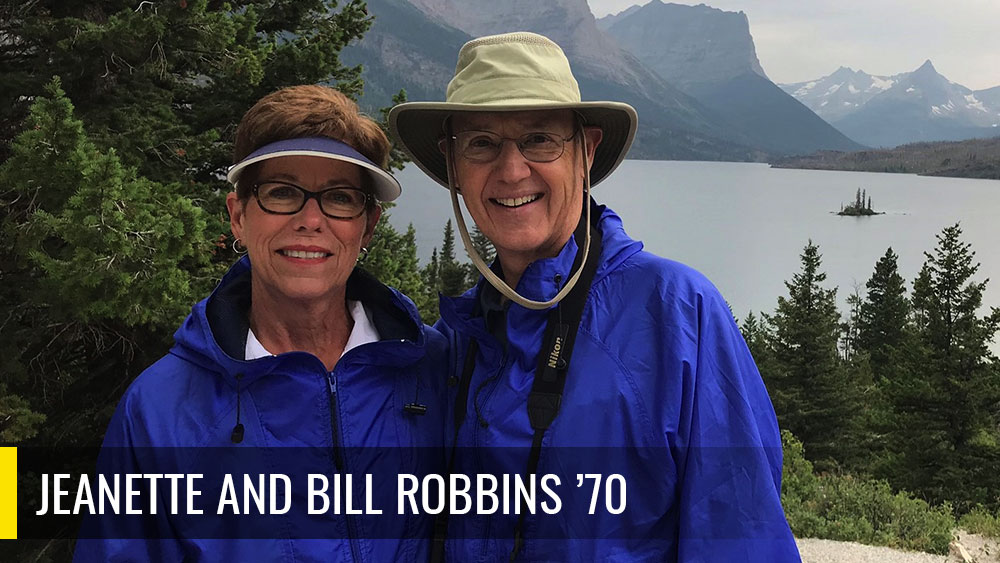 Jeanette and Bill Robbins taking a picture outside in front of mountains. 