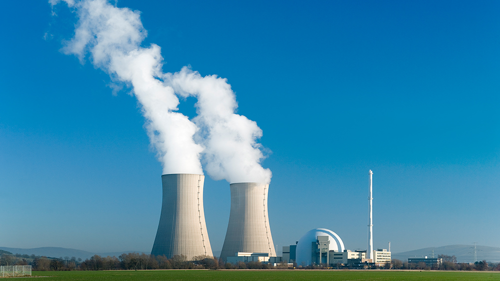 Two nuclear reactor towers with white smoke coming out of them against a blue sky.