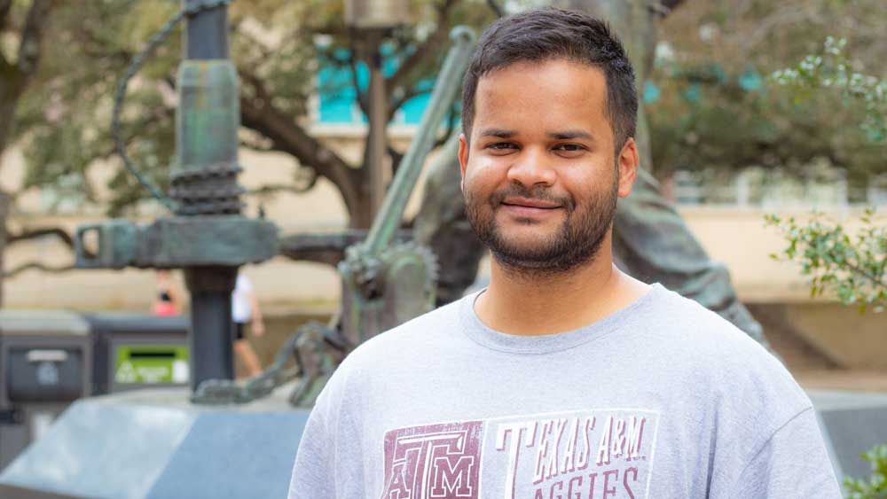 Aditya Chakravarty, smiling and seated in front of statue on Texas A&amp;M University campus