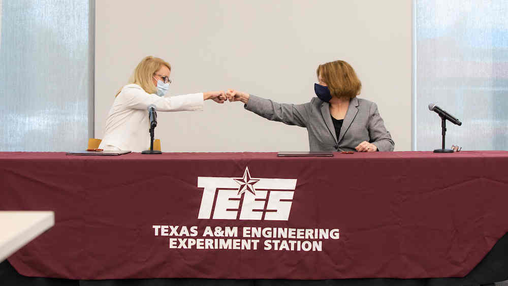 Seated next to one another at a table, Bridget Lauderdale and Dr. M. Katherine Banks do a fist bump to celebrate the Lockheed Martin master research agreement the two women have just signed.