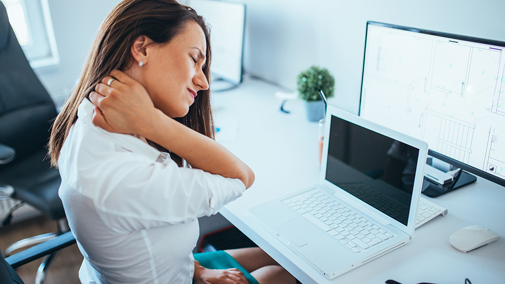 Woman in front to computer screen holds her painful neck. 